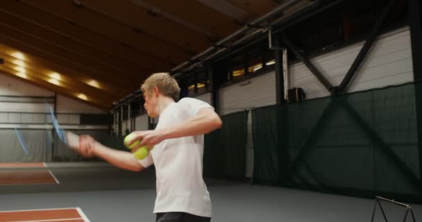 Mladý muž hází tenisové míčky s raketou přes síť jeden po druhém — Stock video