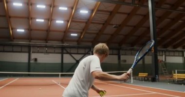 Tenis kortunda tek başına antrenman yapan bir adam, kaleye tenis topu atıyor.