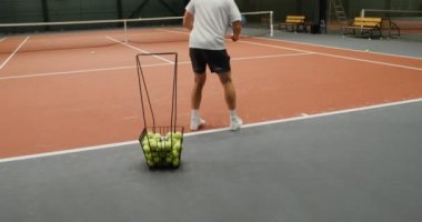 Tenis kortunda tek başına antrenman yapan bir adam, kaleye tenis topu atıyor.