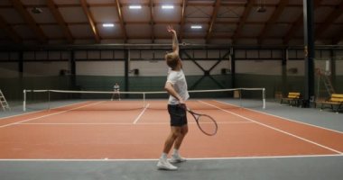 Genç adam ve kadın kapalı tenis kortunda tenis oynuyorlar.