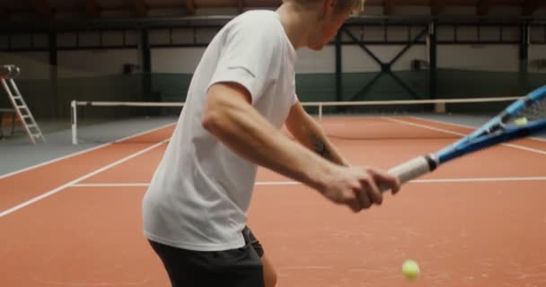 Muž trénuje sám na tenisovém kurtu a háže tenisové míčky přes síť — Stock video
