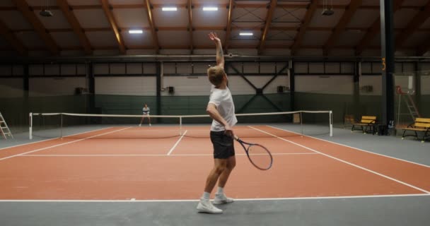 Joven hombre y mujer jugar al tenis en una pista de tenis cubierta — Vídeos de Stock