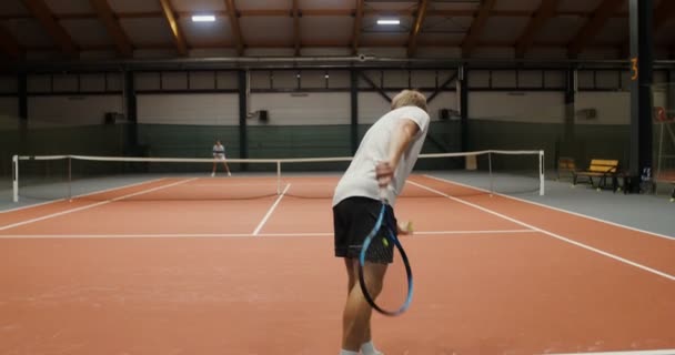 Joven hombre y mujer jugar al tenis en una pista de tenis cubierta — Vídeos de Stock