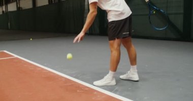 Bir adam tenis takımına başlar, atmadan önce topa vurur.