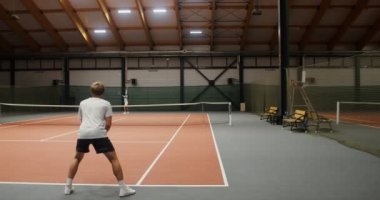 Kapalı tenis kortunda genç bir adamla bir kadın arasında oynanan tenis maçı.