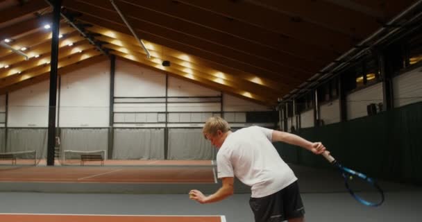 En man startar ett tennisset, slår bollen på golvet innan du kastar — Stockvideo