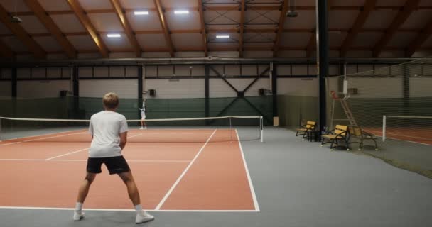 Paired tennis game between a young man and a woman in an indoor tennis court — Stock Video