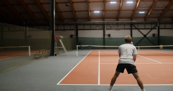 Permainan tenis pasangan antara seorang pria muda dan seorang wanita di lapangan tenis dalam ruangan — Stok Video