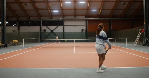 Jóvenes atletas juegan al tenis en una gran sala solos, lanzando la pelota con raqueta — Vídeos de Stock