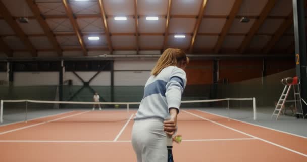 A young woman throws tennis ball over the net with a strong blow of the racket — Stock Video
