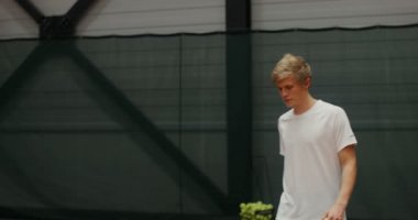 Genç tenisçi ilk topu kapalı tenis kortunda raketle servis ediyor.