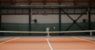 Genç adam ve kadın kapalı tenis kortunda tenis oynuyorlar.