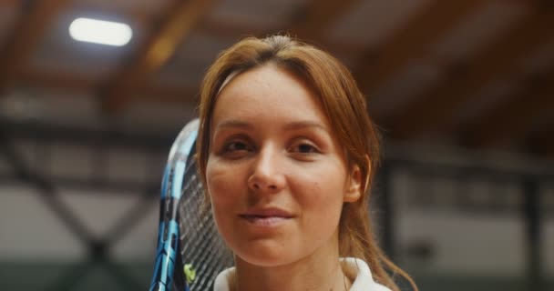 Joven jugadora de tenis sonriendo mirando a la cámara en una pista de tenis — Vídeos de Stock