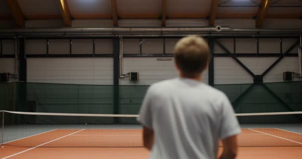 Ung man och kvinna spelar tennis i en inomhus tennisbana — Stockvideo