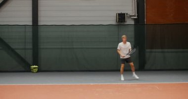 Bir adam partneriyle tenis oynar, topa konsantre olur ve ona vurur.