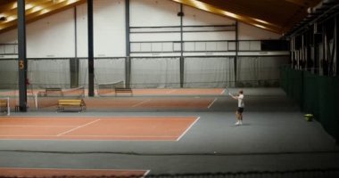 Bir adam partneriyle tenis oynar, topa konsantre olur ve ona vurur.