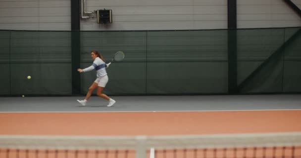 A young woman tennis player runs on the tennis court hitting a tennis ball — Stock Video