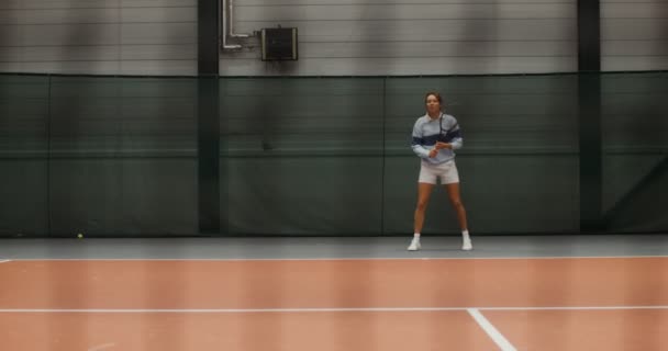 Una giovane tennista corre sul campo da tennis colpendo una palla da tennis — Video Stock