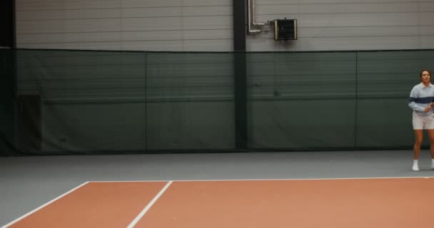 若い女性のテニス選手がテニスボールを打つテニスコートで走ります — ストック動画