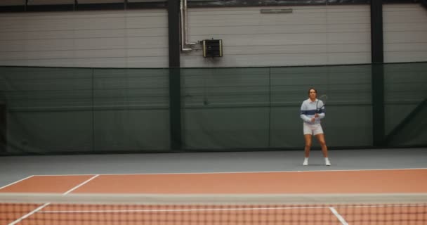 若い女性のテニス選手がテニスボールを打つテニスコートで走ります — ストック動画