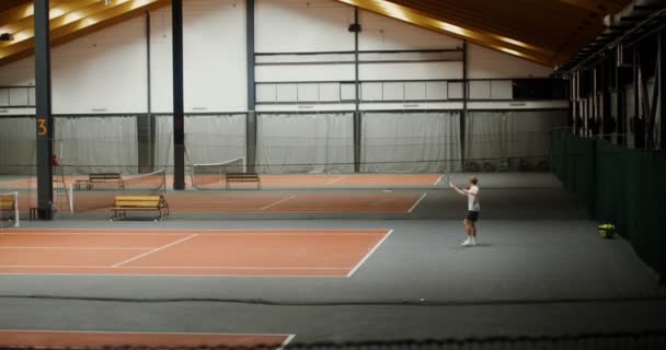 En man spelar tennis med sin partner, koncentrerar sig på bollen och träffar den — Stockvideo