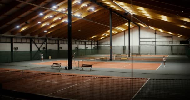 Os jovens estão treinando para jogar tênis em um dos tribunais de um grande ginásio indoor — Vídeo de Stock