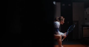 Tenis oynadıktan sonra dinlenen genç bir kadın soyunma odasında bir bankta oturuyor.