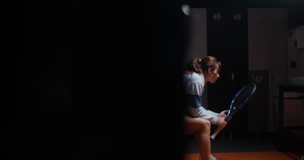 Ung kvinna vilar efter att ha spelat tennis, sitter på en bänk i ett omklädningsrum — Stockvideo