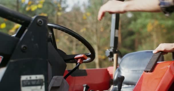 Young man in a baseball cap climbs onto a tractor seat, getting ready for a trip — Stock Video