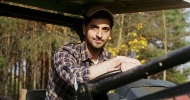 Молодой человек улыбается, глядя в камеру, сидя на сельскохозяйственном автомобиле — стоковое видео