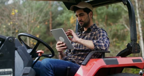 Mladý muž používá tablet, když sedí ve stojící zemědělské mašině — Stock video