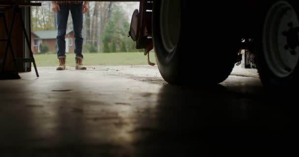 Un hombre entra en un garaje interior acercándose a un tractor, piernas masculinas de cerca — Vídeos de Stock