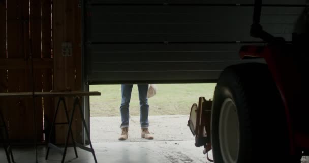 Um homem entra em uma garagem interior se aproximando de um trator — Vídeo de Stock