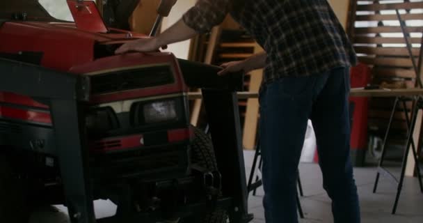 A young man repairs a small agricultural tractor in a wooden barn — Stock Video