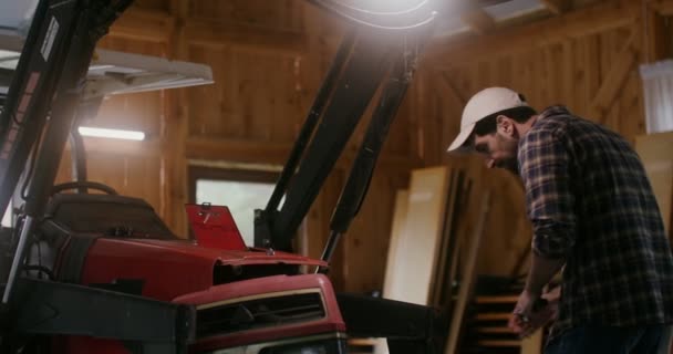 A young man repairs a small agricultural tractor in a wooden barn — Stock Video
