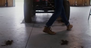 Genç bir adam ahşap bir ahırda küçük bir tarım traktörünü tamir ediyor.