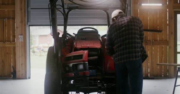Un jeune homme répare un petit tracteur agricole dans une grange en bois — Video