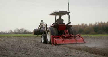 Genç bir çiftçi tarlayı sabanla sürerek bir traktör sürüyor.