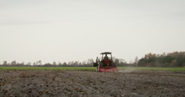 Genç bir çiftçi tarlayı sabanla sürerek bir traktör sürüyor.
