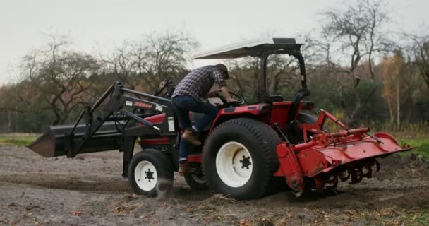 Молодой фермер садится за руль сельскохозяйственной техники и начинает водить — стоковое видео