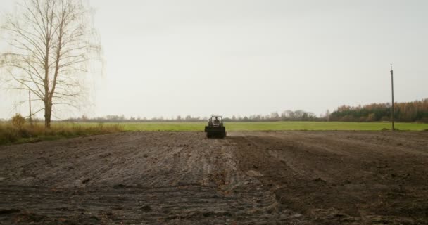 Miespuolinen traktorinkuljettaja ajaa maataloustraktoria, joka kyntää pienen pellon — kuvapankkivideo