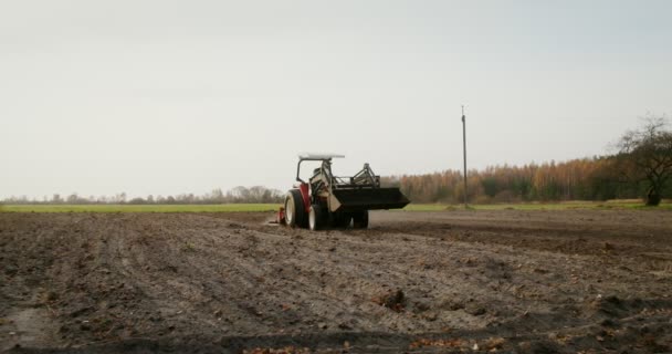 A male tractor driver drives an agricultural tractor plowing a small field — Stock Video