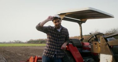 Makineye yaslanmış bir traktör sürücüsü kameraya bakarken gülümsüyor.