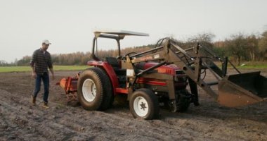 Adamın biri tarladan geçerek traktöre doğru yürür ve kamaradaki koltuğa oturur.