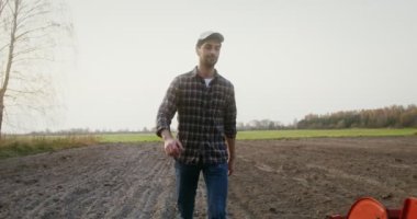 Adamın biri tarladan geçerek traktöre doğru yürür ve kamaradaki koltuğa oturur.