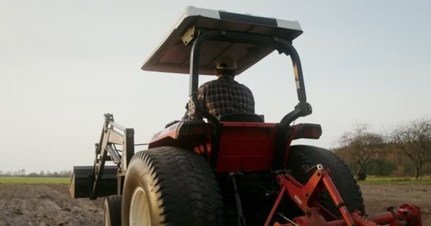 Ein männlicher Traktorfahrer fährt einen landwirtschaftlichen Traktor, der ein kleines Feld pflügt — Stockvideo