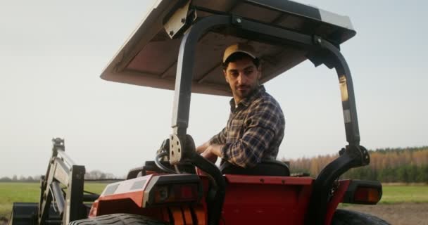 Een mannelijke trekker bestuurder rijdt een landbouwtrekker ploegen een klein veld — Stockvideo