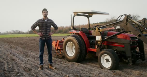 En traktorförare lutar sig mot en maskin och ler när han tittar in i kameran — Stockvideo