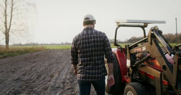Чоловік проходить через оранжеве поле до трактора і сидить на сидінні в кабіні — стокове відео