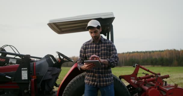 Jeune conducteur de tracteur utilise une tablette appuyée sur un tracteur agricole moderne — Video